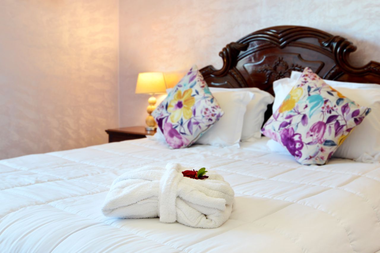 Hotel bed with white bathrobe and a red flower