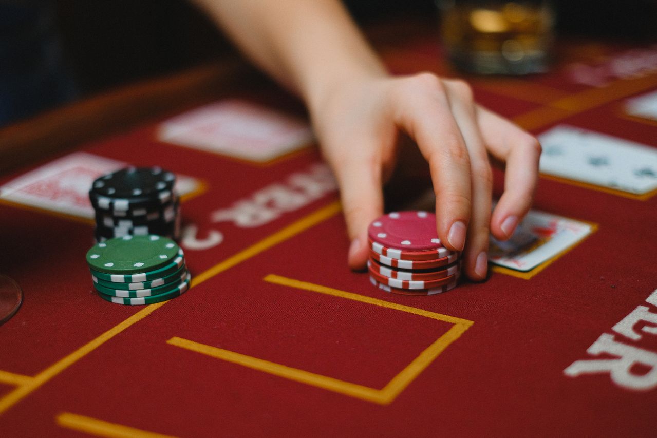 Hand placing chips on a red gaming table beside a cocktail glass